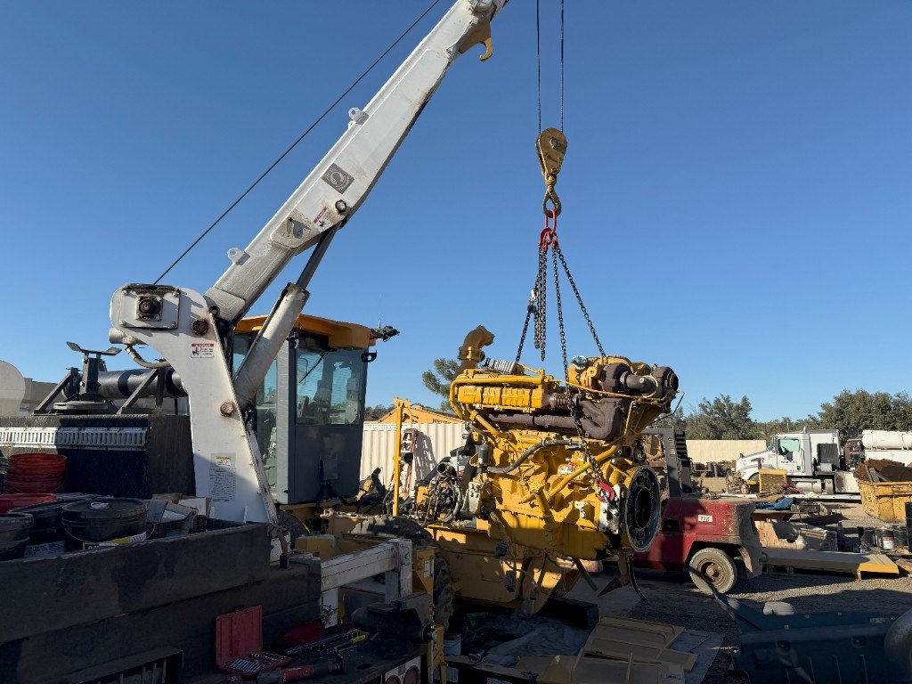 Large diesel engine lifted by crane at a repair yard